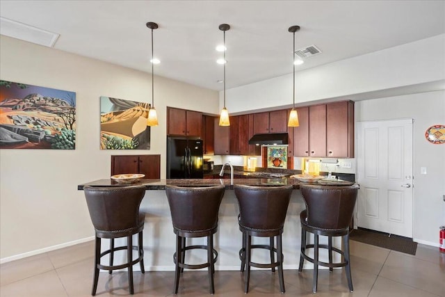 kitchen featuring black fridge, tile patterned flooring, pendant lighting, a kitchen bar, and a kitchen island with sink