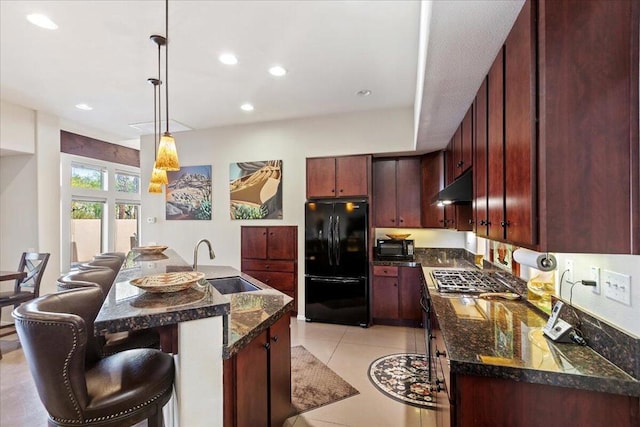 kitchen featuring pendant lighting, a kitchen island with sink, black appliances, sink, and a breakfast bar area