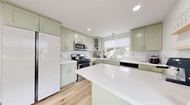 kitchen featuring backsplash, stainless steel appliances, sink, light hardwood / wood-style flooring, and hanging light fixtures