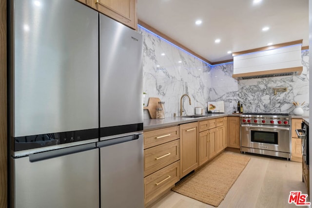 kitchen with light brown cabinetry, sink, light hardwood / wood-style flooring, custom range hood, and stainless steel appliances