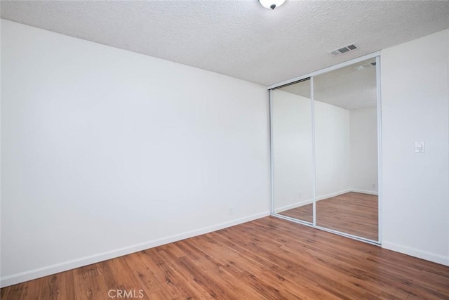 unfurnished bedroom with a textured ceiling, hardwood / wood-style flooring, and a closet