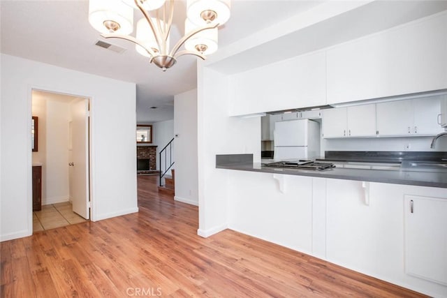 kitchen featuring light wood-type flooring, white refrigerator, white cabinets, and hanging light fixtures