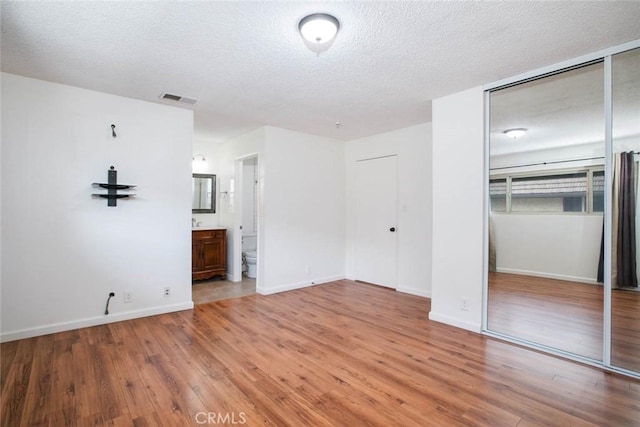 unfurnished bedroom featuring a textured ceiling, connected bathroom, hardwood / wood-style flooring, and a closet