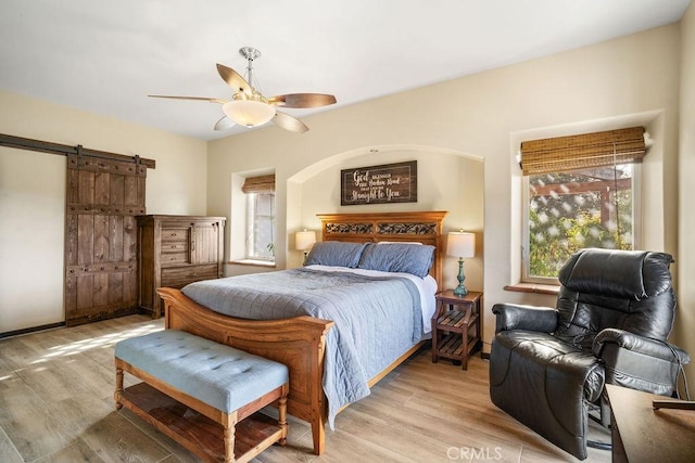 bedroom featuring ceiling fan, a barn door, and light hardwood / wood-style flooring