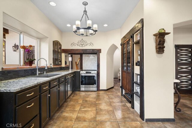 kitchen featuring kitchen peninsula, pendant lighting, light stone countertops, stainless steel stove, and sink