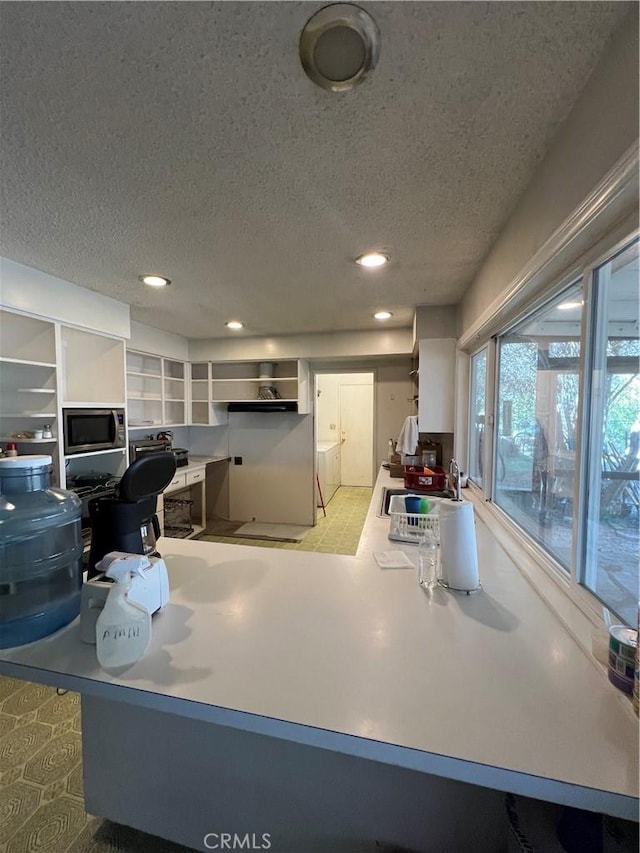 kitchen featuring white cabinets, sink, stainless steel microwave, and a textured ceiling