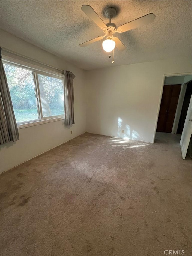 empty room with carpet flooring, ceiling fan, and a textured ceiling