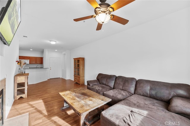 living room featuring ceiling fan, light wood-type flooring, and a fireplace