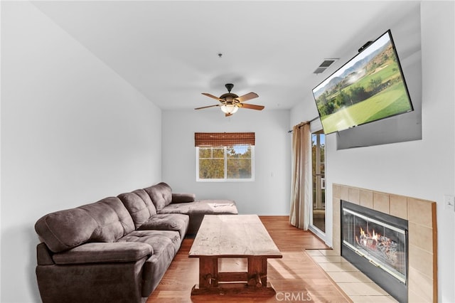 living room with light hardwood / wood-style floors, ceiling fan, and a tiled fireplace