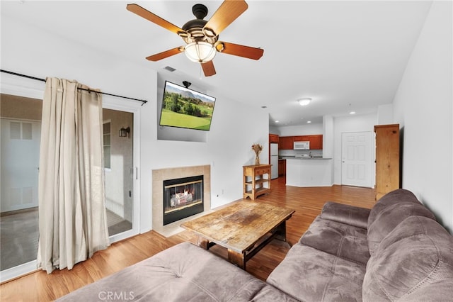 living room featuring a tile fireplace, light hardwood / wood-style floors, and ceiling fan