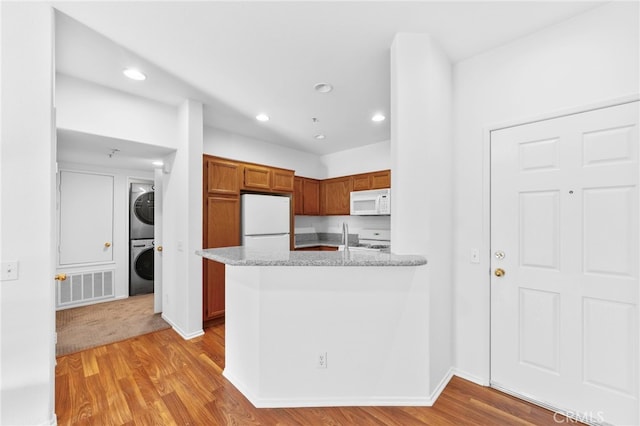 kitchen with stacked washing maching and dryer, light stone counters, white appliances, and light wood-type flooring