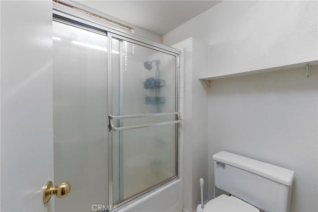 bathroom featuring toilet and shower / bath combination with glass door