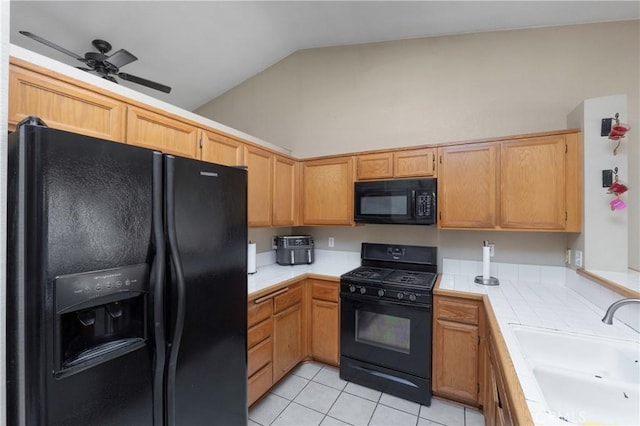 kitchen featuring tile counters, sink, lofted ceiling, light tile patterned floors, and black appliances