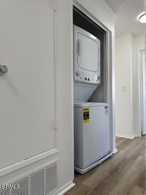 laundry room with stacked washing maching and dryer, a textured ceiling, and wood-type flooring