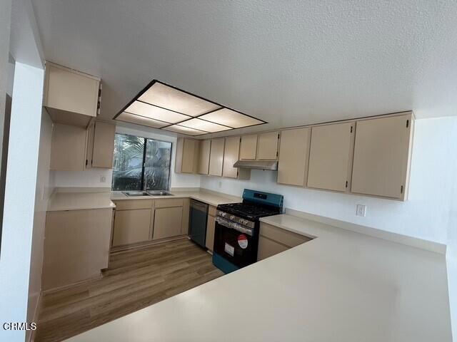 kitchen with a textured ceiling, sink, black appliances, hardwood / wood-style flooring, and cream cabinetry