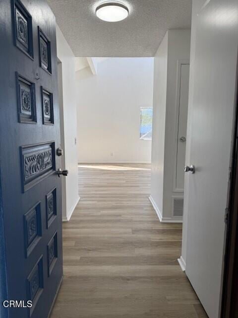 corridor featuring beamed ceiling, a textured ceiling, and light wood-type flooring