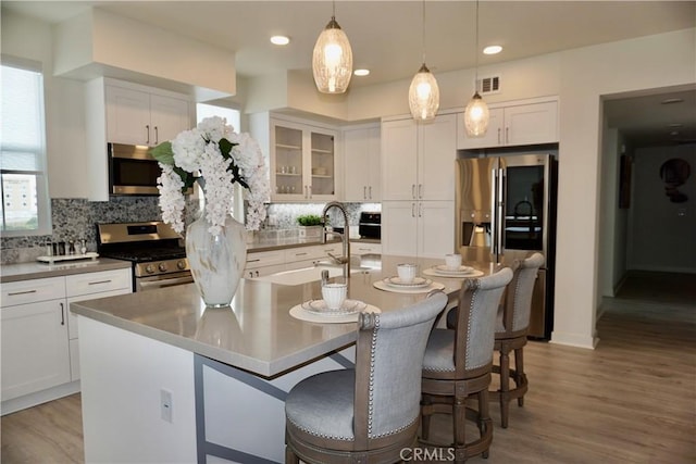 kitchen featuring white cabinets, appliances with stainless steel finishes, a center island with sink, and decorative backsplash