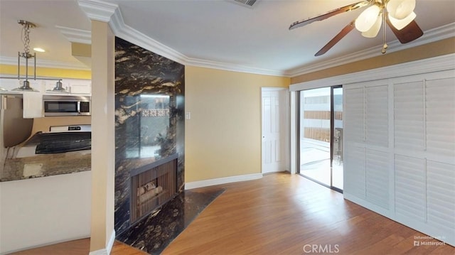 interior space with ceiling fan, wood finished floors, a high end fireplace, baseboards, and ornamental molding