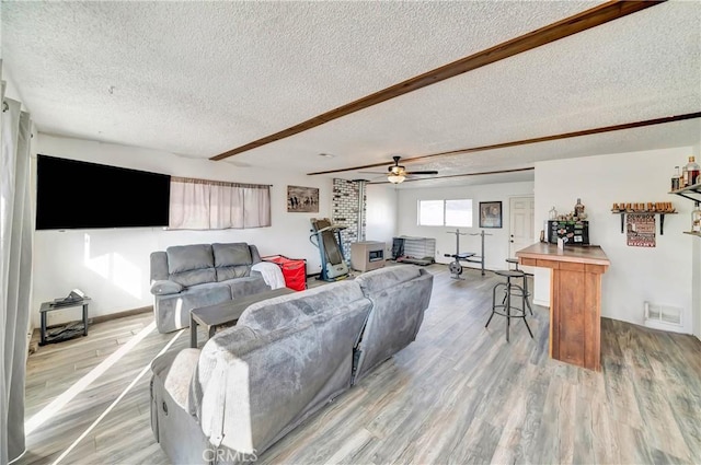 living room with light wood-type flooring, beam ceiling, a textured ceiling, and ceiling fan