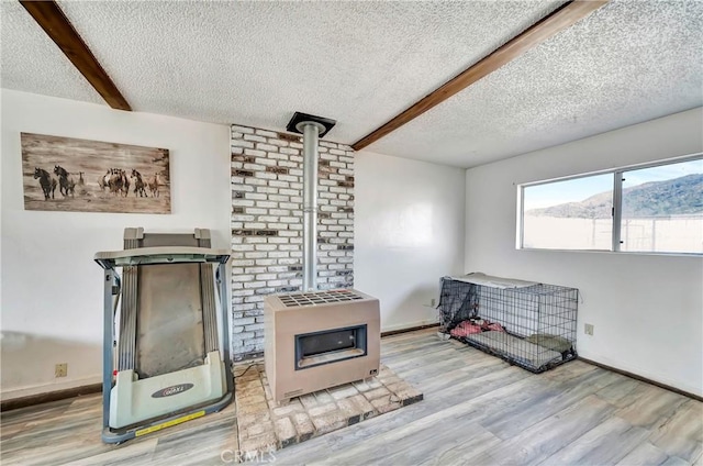 kitchen with beamed ceiling, a textured ceiling, light hardwood / wood-style floors, and a wood stove