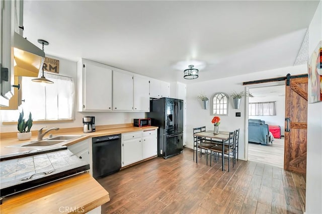 kitchen with white cabinetry, dark wood-type flooring, a barn door, pendant lighting, and black appliances