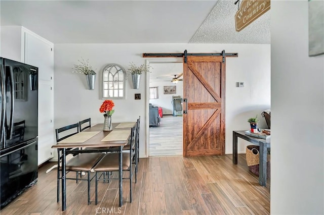 dining space with a barn door, ceiling fan, hardwood / wood-style floors, and a textured ceiling