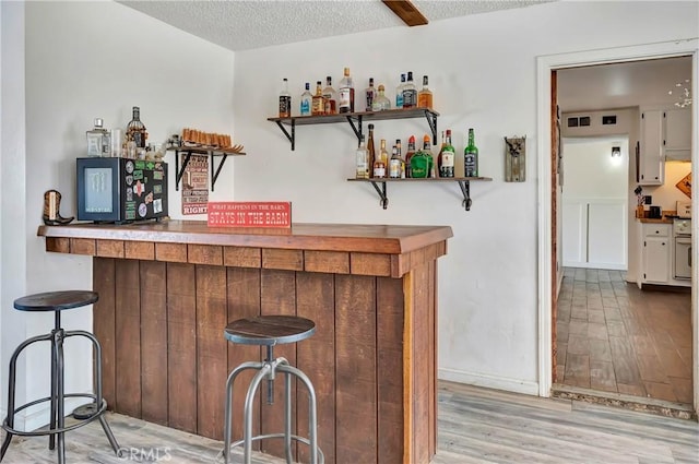 bar with a textured ceiling and light hardwood / wood-style flooring