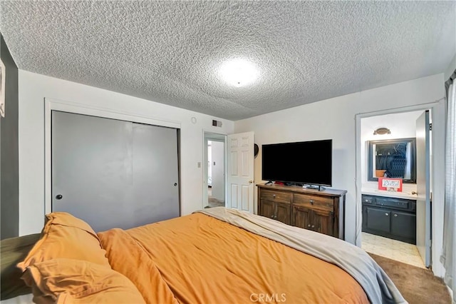 carpeted bedroom with ensuite bathroom, a closet, and a textured ceiling