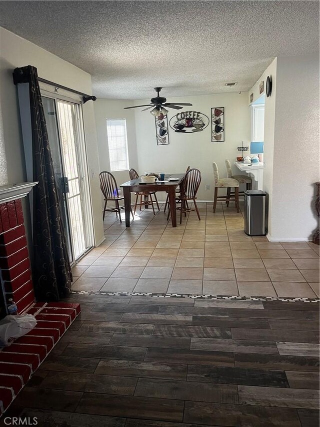 tiled dining area with a textured ceiling, a brick fireplace, and ceiling fan