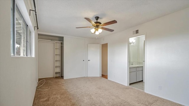 unfurnished bedroom with ceiling fan, light colored carpet, a textured ceiling, connected bathroom, and a closet