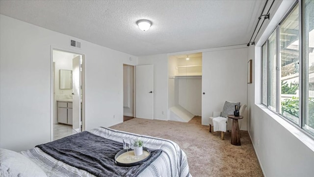 bedroom featuring a spacious closet, a textured ceiling, ensuite bath, light carpet, and a closet