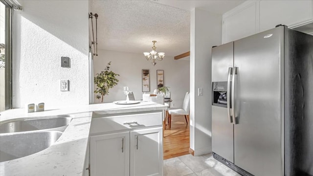 kitchen featuring sink, white cabinets, stainless steel fridge with ice dispenser, a textured ceiling, and a notable chandelier