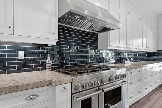 kitchen with double oven range, ventilation hood, white cabinetry, and decorative backsplash