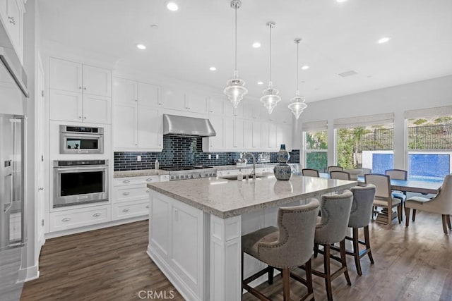 kitchen featuring a center island with sink, pendant lighting, sink, white cabinetry, and light stone counters