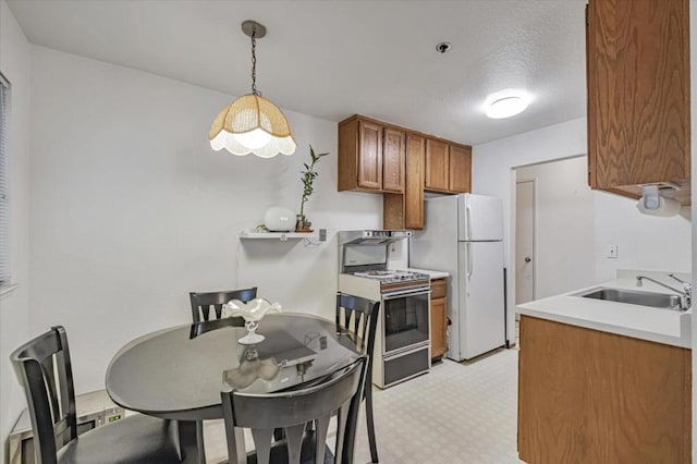 kitchen featuring a textured ceiling, white appliances, sink, and hanging light fixtures