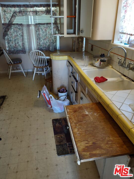 kitchen with tasteful backsplash, white cabinetry, tile counters, and sink