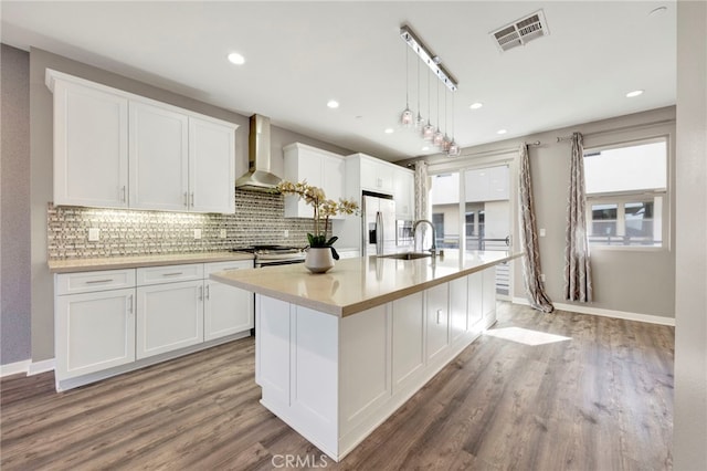 kitchen with white cabinetry, wall chimney exhaust hood, a kitchen island with sink, and wood-type flooring