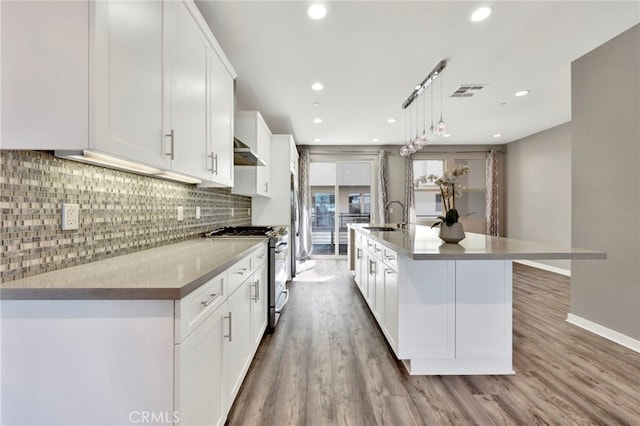 kitchen featuring pendant lighting, a large island with sink, white cabinets, light wood-type flooring, and gas stove