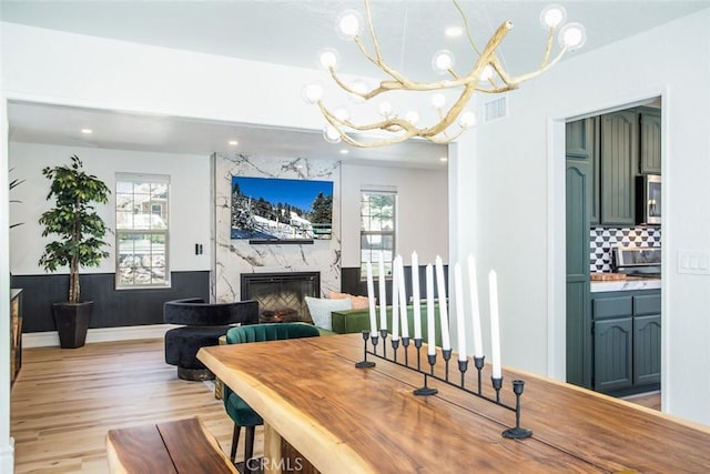 dining space with a high end fireplace, light hardwood / wood-style floors, and an inviting chandelier