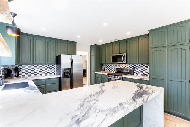 kitchen featuring light stone countertops, appliances with stainless steel finishes, tasteful backsplash, sink, and green cabinetry