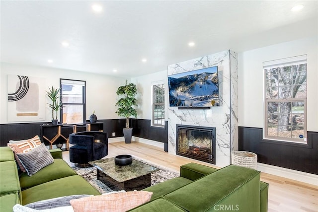 living room featuring a high end fireplace, light hardwood / wood-style floors, and wooden walls