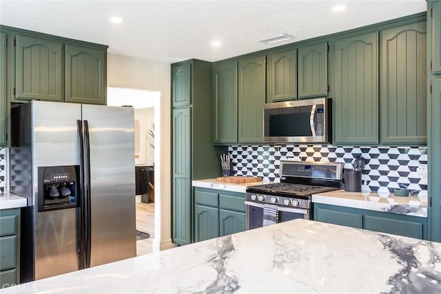 kitchen featuring decorative backsplash, stainless steel appliances, light stone counters, and green cabinets