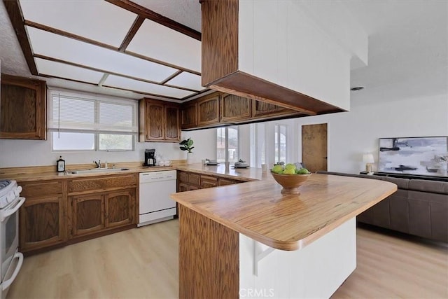 kitchen with kitchen peninsula, sink, white appliances, and light wood-type flooring