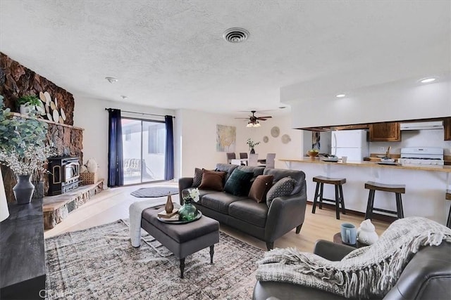 living room featuring a textured ceiling, light hardwood / wood-style floors, a wood stove, and ceiling fan