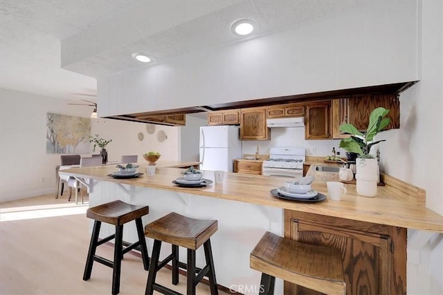 kitchen with kitchen peninsula, a breakfast bar, a textured ceiling, white appliances, and sink