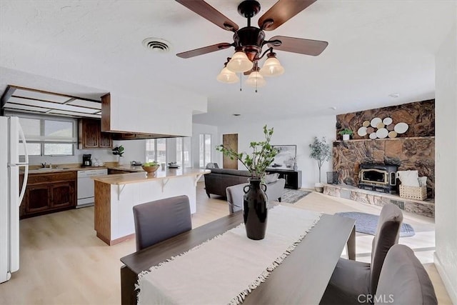 dining space featuring ceiling fan, a wood stove, sink, and light hardwood / wood-style flooring