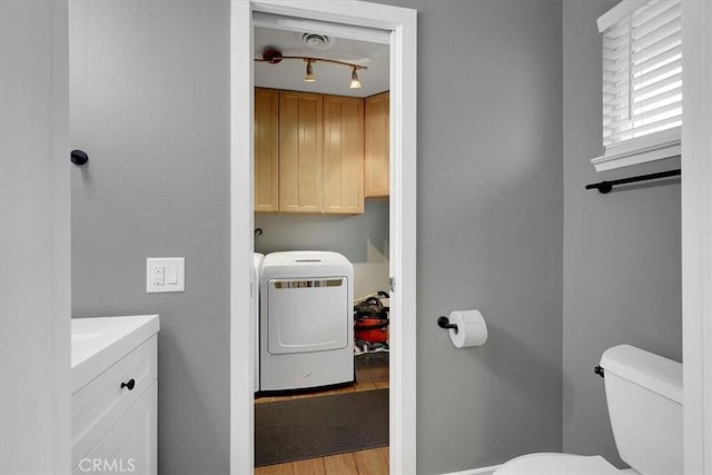 half bathroom featuring toilet, wood finished floors, vanity, washer and clothes dryer, and track lighting