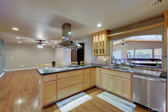 kitchen with dark countertops, a peninsula, island exhaust hood, stainless steel appliances, and light brown cabinetry