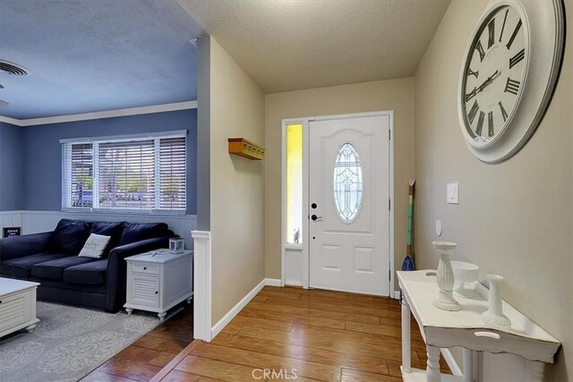 entryway featuring light hardwood / wood-style flooring, ornamental molding, and a textured ceiling