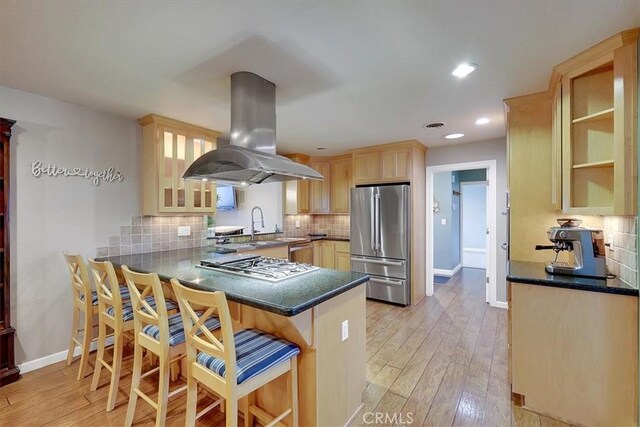 kitchen with a peninsula, appliances with stainless steel finishes, light brown cabinetry, light wood finished floors, and island exhaust hood